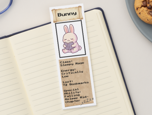 Bookmark with a cartoon bunny design on a notebook next to cookies and glasses.