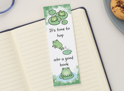 Bookmark with frog design and text on a notebook next to cookies and glasses.